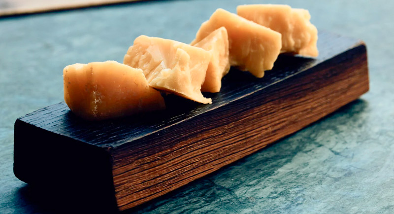 Cuñas de queso artesano madurado (tipo Parmesano) presentadas sobre tabla oscura.