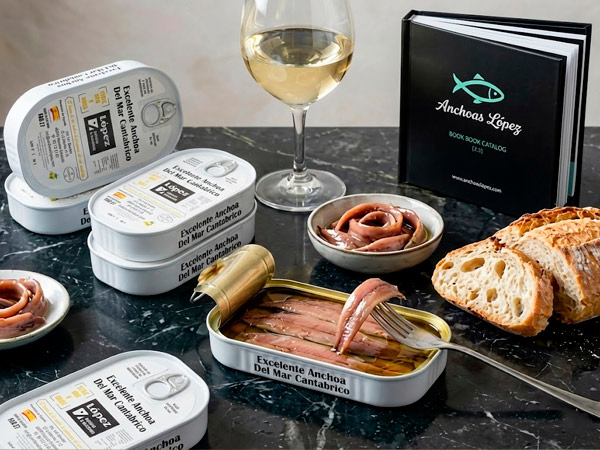 Latas de anchoas López sobre mesa de mármol con pan y copa de vino blanco.