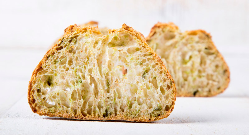 Hogaza de pan de masa madre con especialidades (tipo pistacho o hierbas) rebanada para servicio.