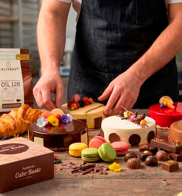 Pastelero ultimando la presentación de un surtido de pastelería premium de Cabo Busto y chocolates Callebaut, incluyendo tartas semifrías, macarons y bombones para hostelería